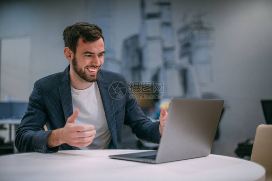 当代青年商人在一台工作笔记本电脑上的肖像在现代办公室内地穿夹克的英俊男士图片