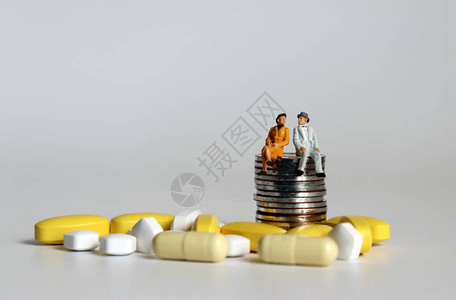一对老微型夫妇和药丸坐在一堆硬币上老龄化社会对老年人医疗保背景图片