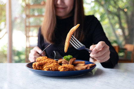女手用刀叉在餐厅吃薯条和炸鸡的近距离画面图片