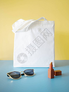 模拟设计袋概念空白色手提袋帆布面料与太阳镜和口红在黄色蓝背景为夏季女时尚主题空的生态购图片