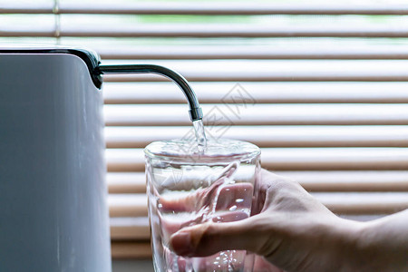男子将水从净水器或滤水器倒入饮用玻璃杯中饮用前的水净化和使水纯净健康人生活方式概念图片