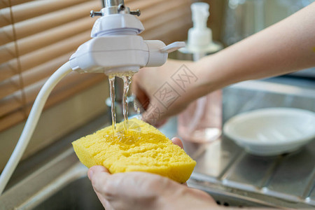 女人在黄色海绵上使用洗碗液关闭管家在水槽里洗脏盘子家政和日常作业概念图片