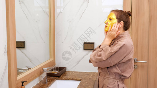 穿浴袍的漂亮女人戴着化妆面罩在浴室侧观下确实在镜图片