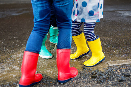 三个孩子蹒跚学步的女孩和两个男孩穿着红色黄色和绿色雨靴图片