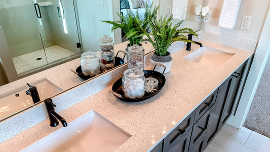 全景瓷砖地板橱柜上方的白色台面上带黑色水龙头的两个水槽浴室内还可以看到托盘罐子植物镜子图片