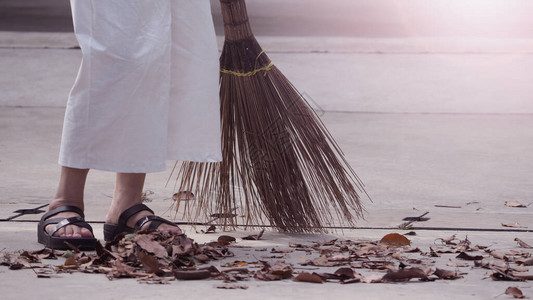 妇女用长木扫帚在水泥地板上擦干叶图片
