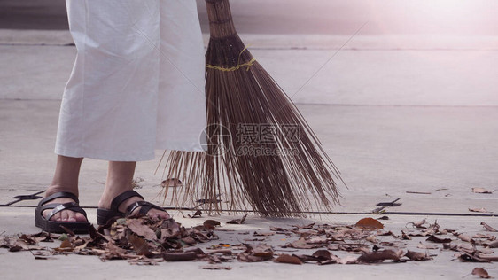 妇女用长木扫帚在水泥地板上擦干叶图片
