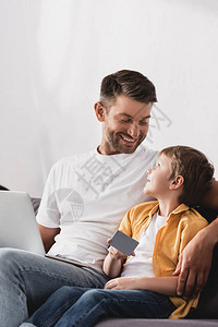 快乐的父亲用笔记本电脑看着微笑的儿子图片