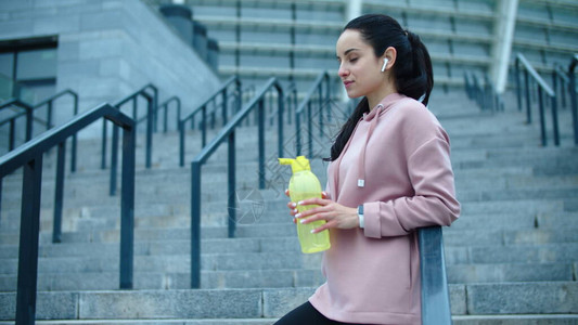 运动型女孩从户外健身瓶喝水运动员女人在慢动作喝水口渴的女人戴着耳机图片