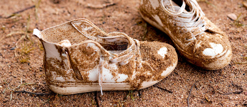脏丢的白色运动鞋躺在沙子里高质量的照片图片