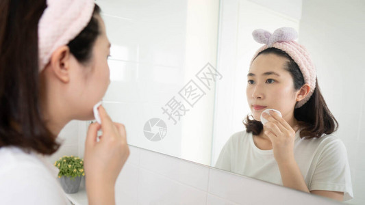 美丽的亚洲女在镜子浴室前用面部棉垫将化妆品从脸上抹去美容和皮肤护理常规图片