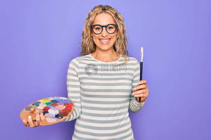 年轻漂亮的金发艺术家女用画笔和调色板画图片