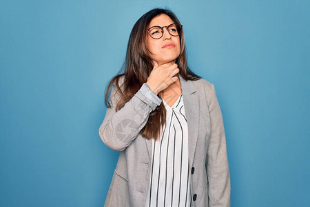 年轻的西班牙裔女商人戴着眼镜站在蓝色孤立的背景上摸着脖子疼喉咙痛流感图片