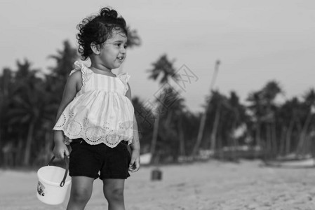 俏皮的漂亮印度女孩儿童婴儿在海滩边玩沙包并给背景图片
