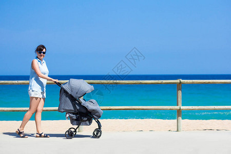 育儿和旅行概念年轻母亲在夏日海滩推婴图片