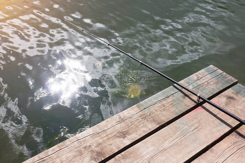 一根钓鱼竿躺在一个悬在水面上的木墩上渔夫的一天的概念夏季和秋季的图片
