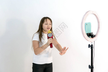 一个手里拿着麦克风的少女一边唱歌一边拍视频自拍手机安装在三脚架上图片