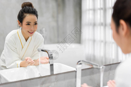 在浴室的镜子前用水洗干净脸的欢快美丽漂亮的亚洲女人的微笑肖像图片