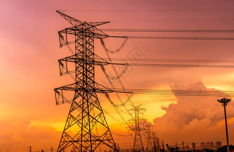 具有橙色日落天空和城市景观现代办公楼背景的高压电塔和输电线路电塔城市的电力和能源背景图片