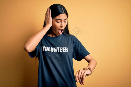 年轻漂亮的西班牙裔女穿着志愿者T恤作为社会慈善道德看着手表时间担图片