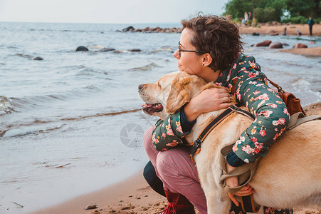 一个女孩和一只拉布多猎犬在沙滩上拥抱图片