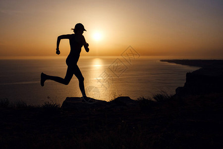 马拉松,在海边的路上跑步的健身女人的侧面图日落时在海滨长廊上训练