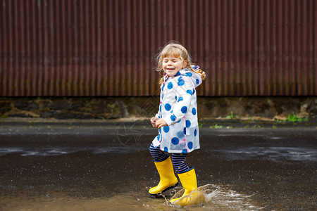 下雨tubiao蹒跚学步的小女孩穿着黄色雨靴背景