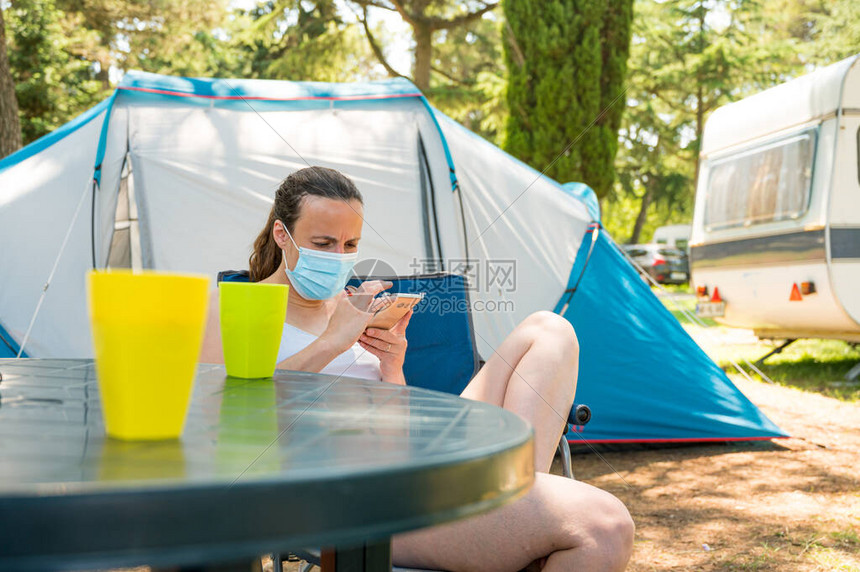 女在露营帐篷前戴面罩检查她的智能手机图片