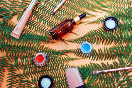 裸色背景上的热带树叶包裹着化妆品面部油和皮肤的天然产品吸管瓶口红彩图片