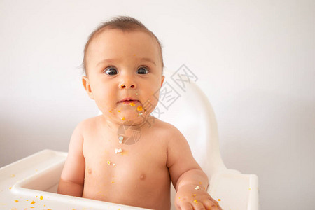 一个可爱又肮脏的6个月的小女孩坐在婴儿椅子上吃东西的时候吃饭图片