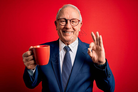 高级灰色头发的商人喝着一杯热咖啡喝着红底咖啡用手指签好牌子图片