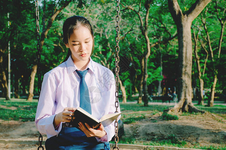 穿着校服阅读书的可爱少女坐在公园秋图片