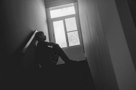 剪影悲伤的年轻人坐在黑暗中的楼梯上图片