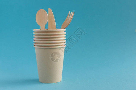 生态友好型一次纸杯和用蓝背景的木勺叉子和刀制成的餐具图片