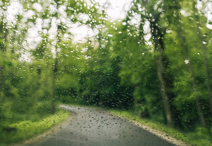 模糊的背景与雨滴落在玻璃和路上的汽车上透过车窗的路景因大雨而模糊雨中驾图片