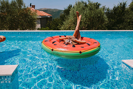 度假时穿着泳装的感女在时分躺在户外游泳池的充气床垫上背景图片