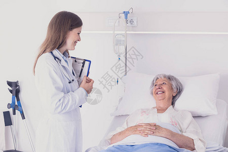 医生或护士在医院的病房巡诊期间与一位高级女病人交谈图片