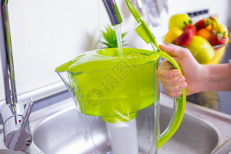 厨房中妇女填水过滤罐饮用水自来水净化和软图片
