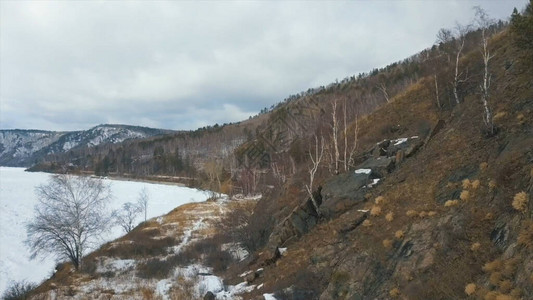 白雪皑的冬季河流和枯黄草枯的岩坡的美丽景色在冬日的雪山环绕的河流冰背景图片