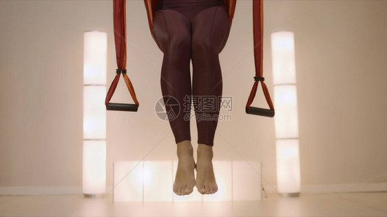 无法认出的女人把腿放到瑜伽带上的特写镜头关闭在健身工作室的吊床上练习瑜伽的女运动员在课堂上练习飞行瑜图片