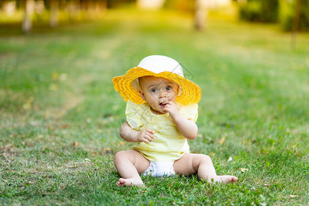 一个8个月大的小女孩夏天穿着黄色的夏装和帽子坐在绿草地上图片