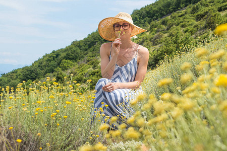 穿着条纹夏装和草帽的年轻女子蹲在超级盛开的野花中图片