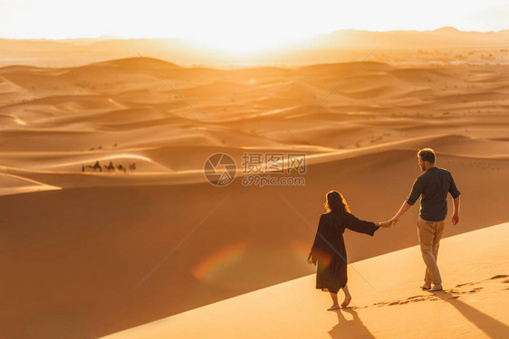 日落时在撒哈拉沙漠行走的情侣图片