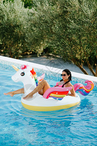 度假时穿着泳装的感女在户外游泳池的充气床垫上放松背景图片