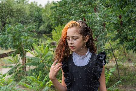 站在雨中的湿女学生女孩湿了在春天或温暖的秋天穿着校服的少年五年级的女孩染发一名女学生溅起水花的肖图片