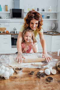 年青母亲有选择地重点在靠近女儿鸡蛋和厨房桌上的饼干模具图片