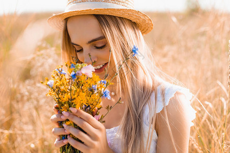 金发女人穿着草帽闻着青草地野图片