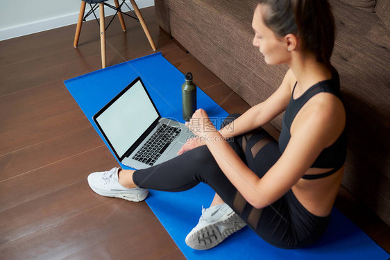 一张身穿黑色紧身裤和上衣的运动女孩的侧面照片正坐在蓝色的瑜伽垫上图片