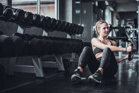 年轻有吸引力的健身女人在健身房用哑铃锻炼的电影色调图片