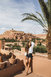 美丽的年轻女子很高兴在摩洛哥旅行背景上的AitBenHaddou古堡穿着白衬衫图片